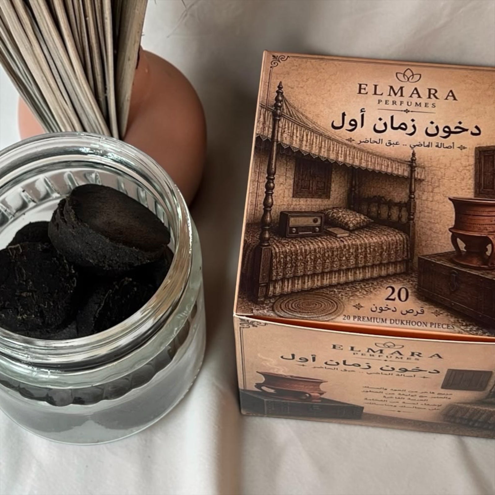 LumaHouse ELMARA PERFUMES Dukhoon incense pieces in a glass jar next to a decorative box with traditional imagery.